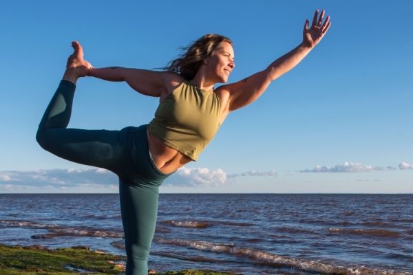 Woman does yoga pose at Canoe Cove beach under a blue sky, PEI